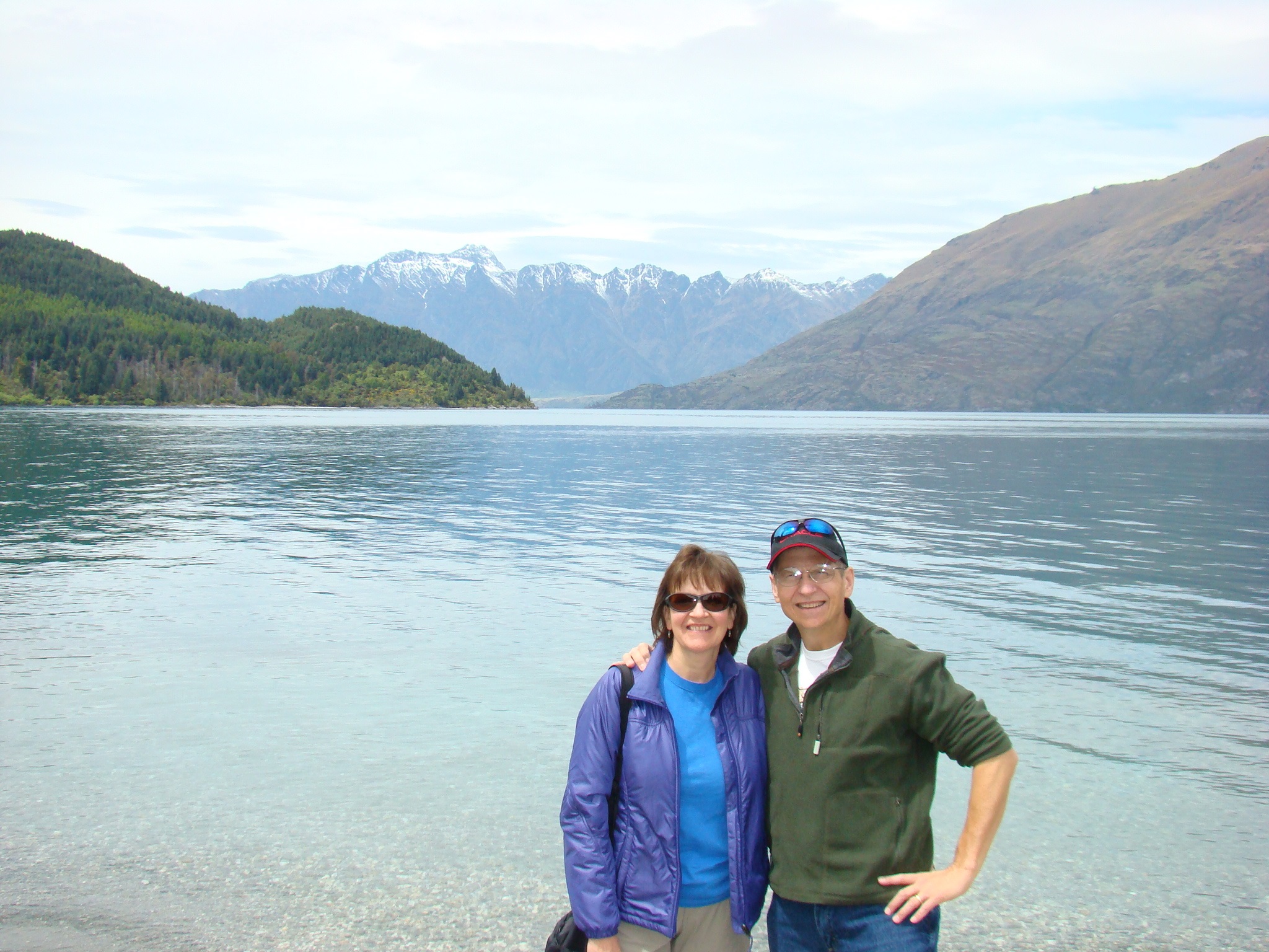 Jim and Ruth taking a photo in front of a lake with mountains in the background