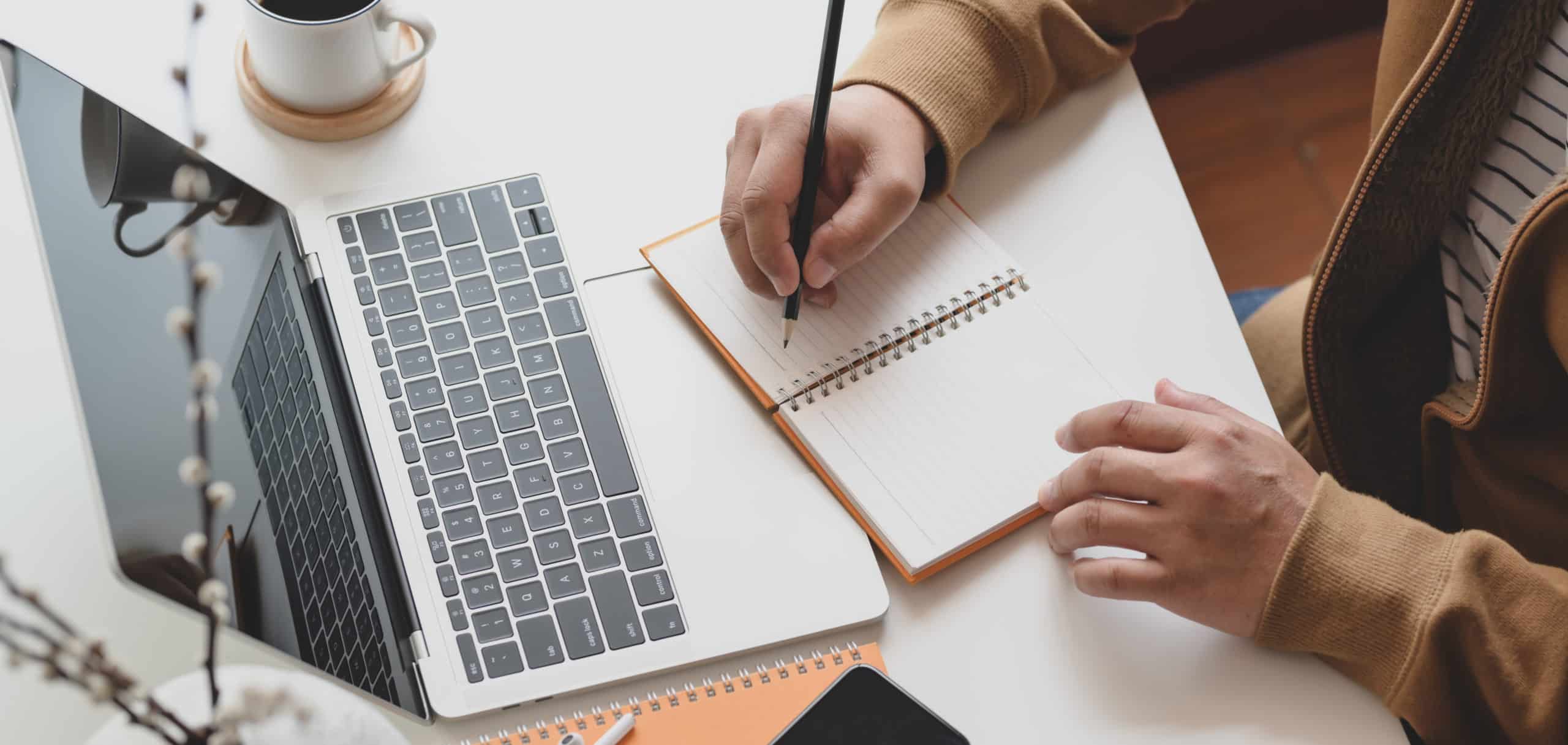 Cropped shot of male freelancer working on his project while writing his ideas on notebook