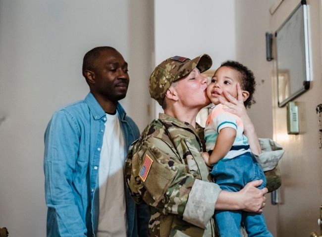 Service member holding a child with family nearby